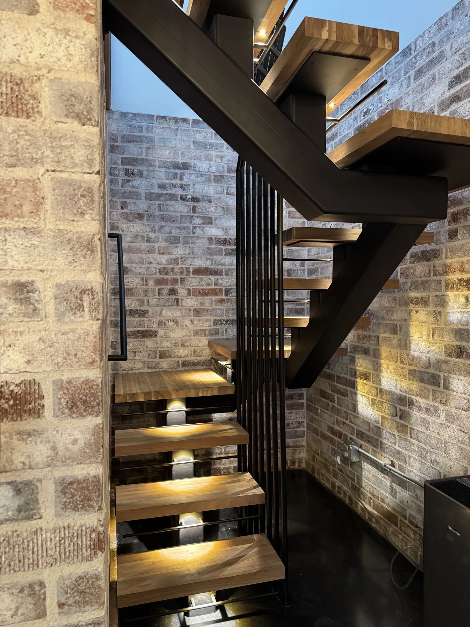 Illuminated walnut stairs descending into the brick cellar